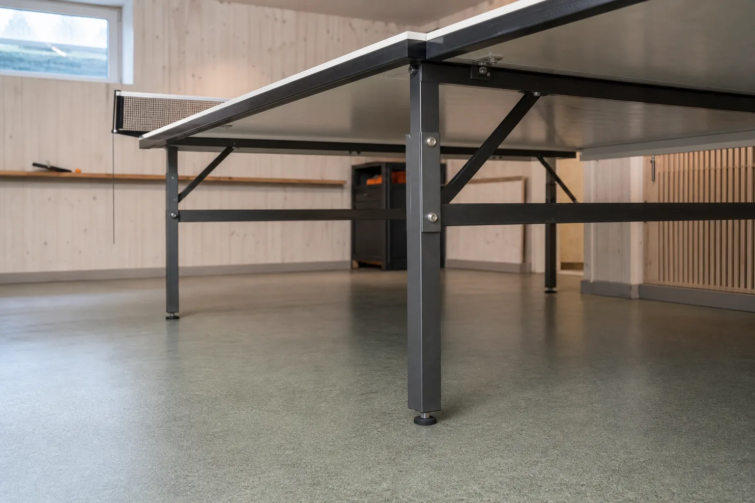 Pingisbordets stöd mot ett plant golv i ett hobbyrum.